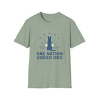 One Nation Under Dog T-Shirt flat lay in sage green, featuring a blue dog silhouette seated before a rising sun with rays and surrounding stars, with bold text reading 'One Nation Under Dog.'