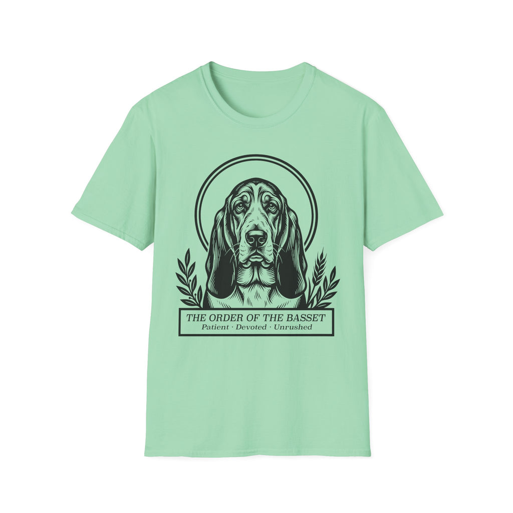 Holy Orders | Basset Hound T-Shirt flat lay on sage green shirt featuring a stained glass style illustration of a Basset Hound depicted as a holy figure with a golden halo and the text 'Holy Orders.'