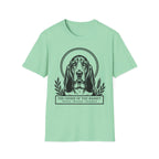 Holy Orders | Basset Hound T-Shirt flat lay on sage green shirt featuring a stained glass style illustration of a Basset Hound depicted as a holy figure with a golden halo and the text 'Holy Orders.'