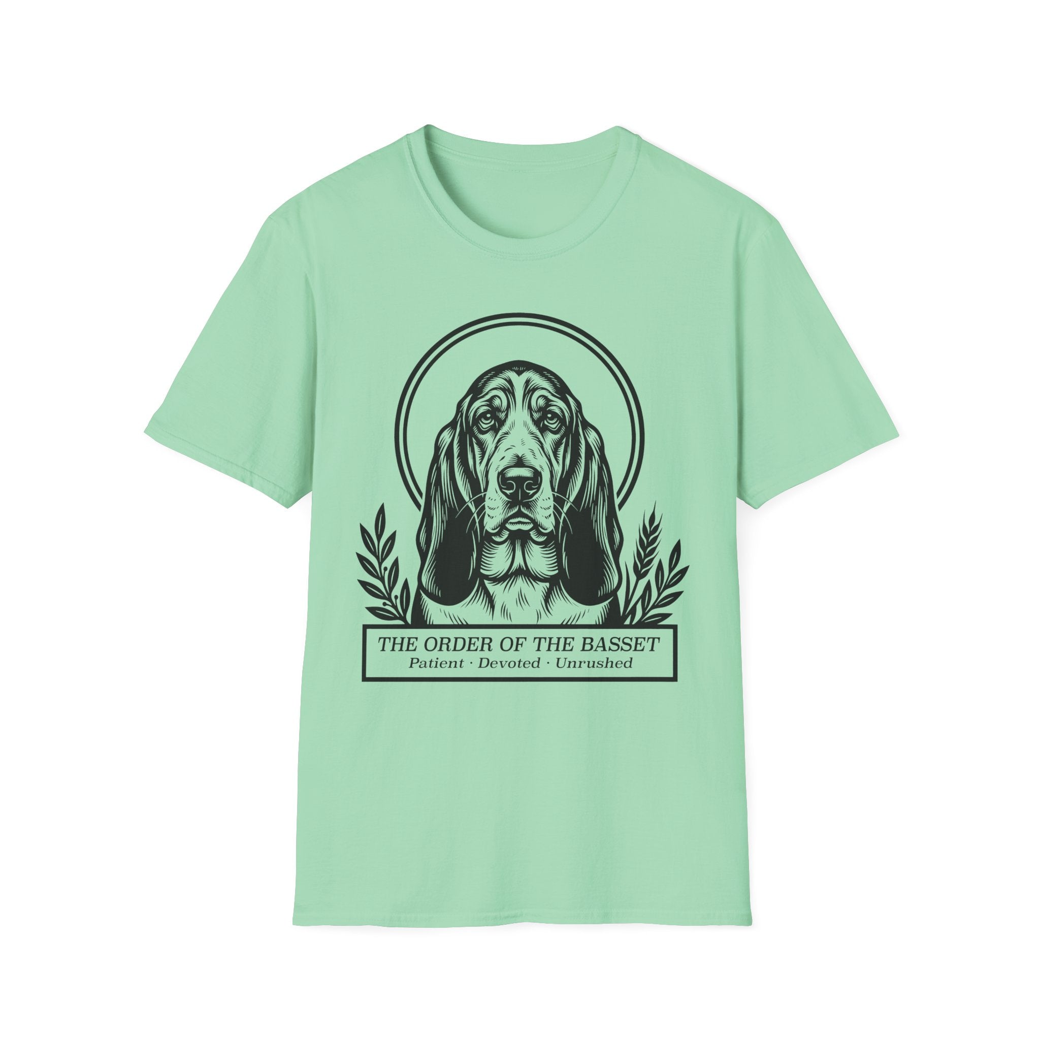 Holy Orders | Basset Hound T-Shirt flat lay on sage green shirt featuring a stained glass style illustration of a Basset Hound depicted as a holy figure with a golden halo and the text 'Holy Orders.'