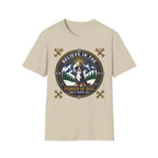 Believe in the Power of Dog Bernese T-Shirt in sand tan, flat lay view showing a circular badge graphic with a halo-wearing Bernese Mountain Dog set against a mountain and forest landscape, with crossed bones and the words 'Loyalty Warmth Love'.