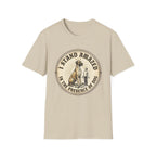 I Stand Amazed Great Dane T-Shirt flat lay in sand, featuring a circular vintage-style graphic of a towering Great Dane with a halo and a small human figure, with text "I Stand Amazed in the Presence of Dog."