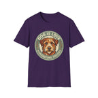 Dog is Love T-Shirt flat lay in purple featuring a vintage circular badge graphic with a scruffy terrier face, "Dog is Love" arched above and "Unconditional Forever" below.