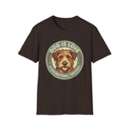 Dog is Love T-Shirt flat lay in dark brown featuring a vintage circular badge graphic with a scruffy terrier face, "Dog is Love" arched above and "Unconditional Forever" below.