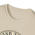 I Stand Amazed Golden Doodle T-Shirt close-up of the neckline and top of the graphic on a sand shirt, showing the ornate circular badge detail with crossed dog bones at the top.