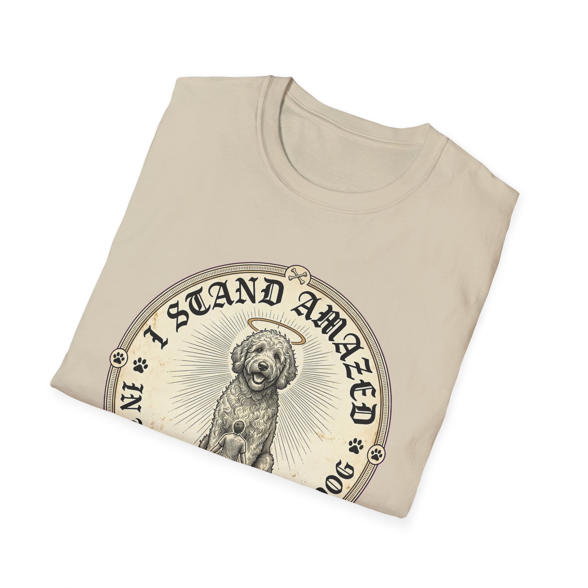 I Stand Amazed Golden Doodle T-Shirt folded view in sand, showing the golden doodle with halo graphic and "I Stand Amazed" lettering prominently on the front chest.