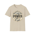 Believe in the Power of Dog Paw T-shirt flat lay in natural sand, featuring a circular vintage badge graphic of a dog paw raised like a fist from clouds above crossed bones, with paw print accents and bold text.
