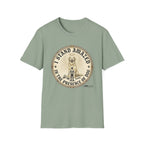 I Stand Amazed Golden Retriever T-Shirt flat lay in sage green, featuring a circular vintage-style graphic of a golden retriever with a halo and rays of light, a small human figure standing beside the dog, with text "I Stand Amazed in the Presence of Dog" and Dogma House branding.