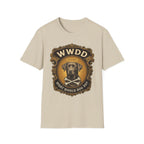 What Would Dog Do Chocolate Lab T-Shirt flat lay on sand, featuring an ornate gold WWDD badge with a halo-wearing chocolate Labrador and crossbones and the text 'What Would Dog Do?'