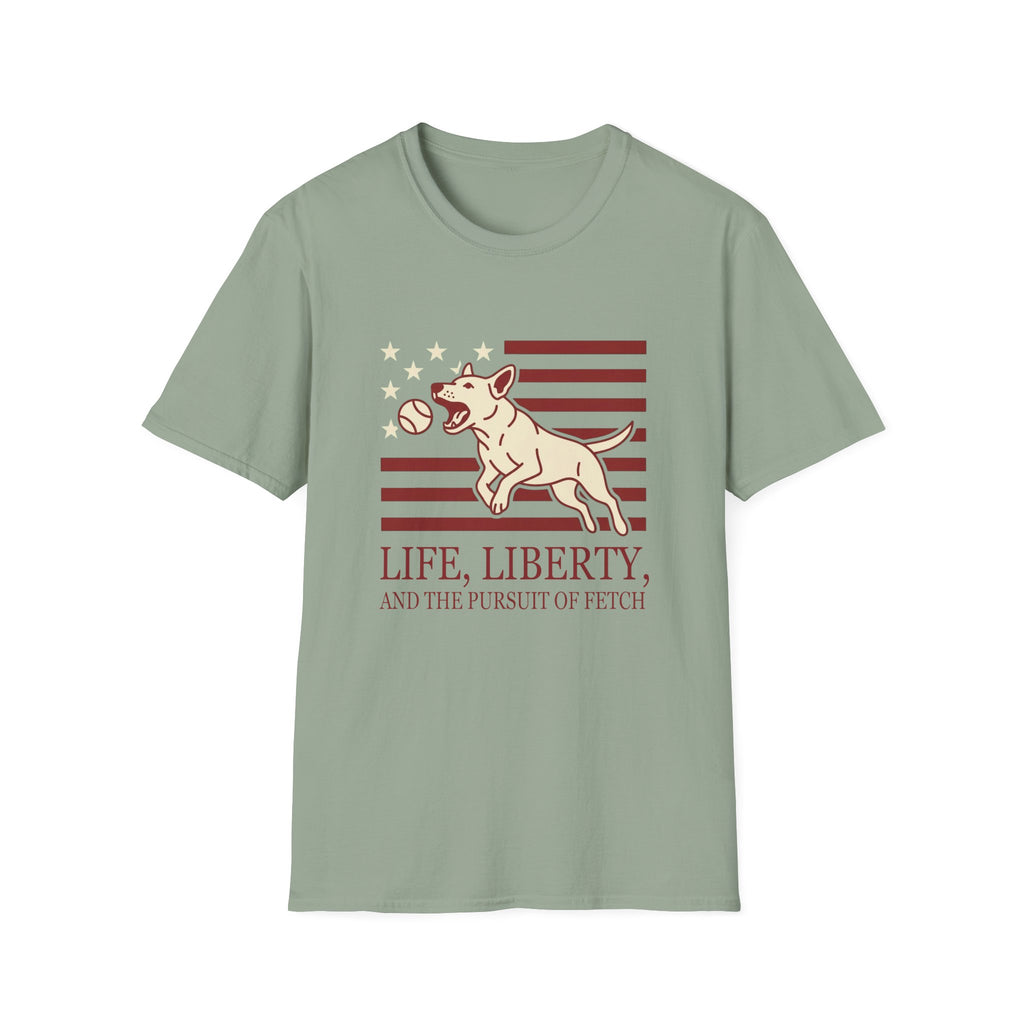 Pursuit of Fetch T-Shirt flat lay in sage green, featuring a leaping dog catching a tennis ball over a flag of red stripes and stars, with text reading 'Life, Liberty, and the Pursuit of Fetch.'