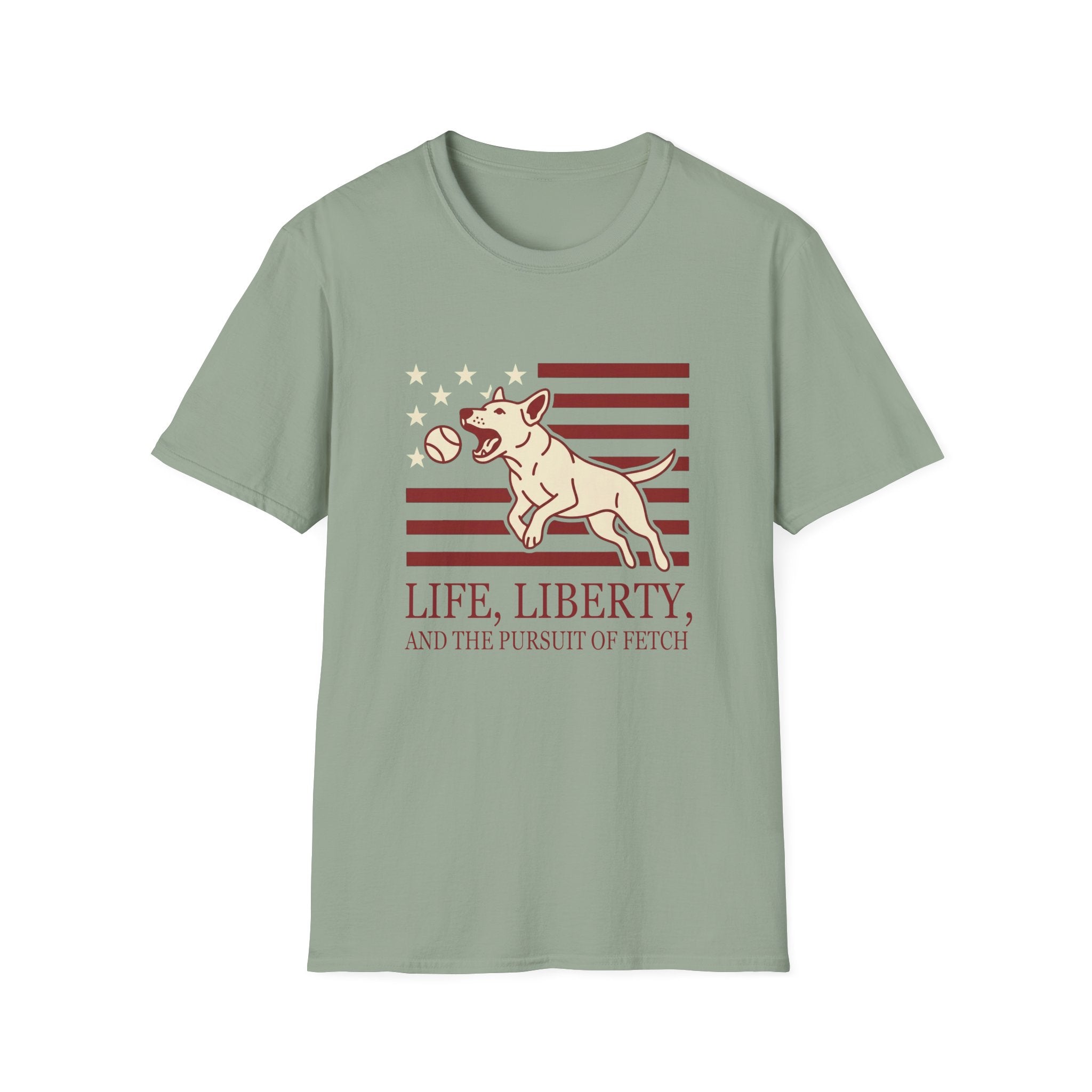 Pursuit of Fetch T-Shirt flat lay in sage green, featuring a leaping dog catching a tennis ball over a flag of red stripes and stars, with text reading 'Life, Liberty, and the Pursuit of Fetch.'