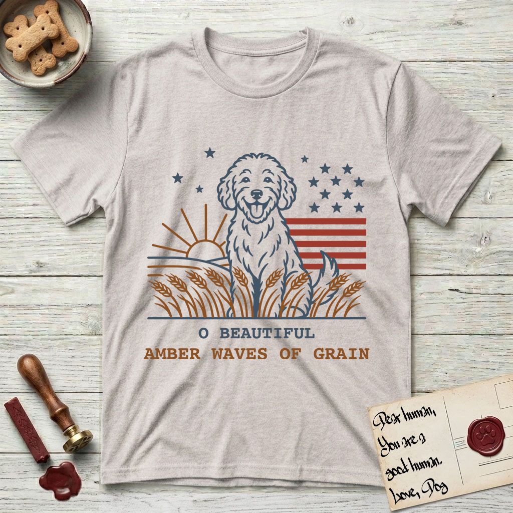 Amber Waves of Grain T-Shirt flat lay in Ice Grey, featuring a faded vintage-Americana line-art Goldendoodle sitting in a wheat field with a rising sun, scattered stars, and red flag stripes, above “O Beautiful / Amber Waves of Grain” lettering.