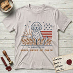 Amber Waves of Grain T-Shirt flat lay in Ice Grey, featuring a faded vintage-Americana line-art Goldendoodle sitting in a wheat field with a rising sun, scattered stars, and red flag stripes, above “O Beautiful / Amber Waves of Grain” lettering.