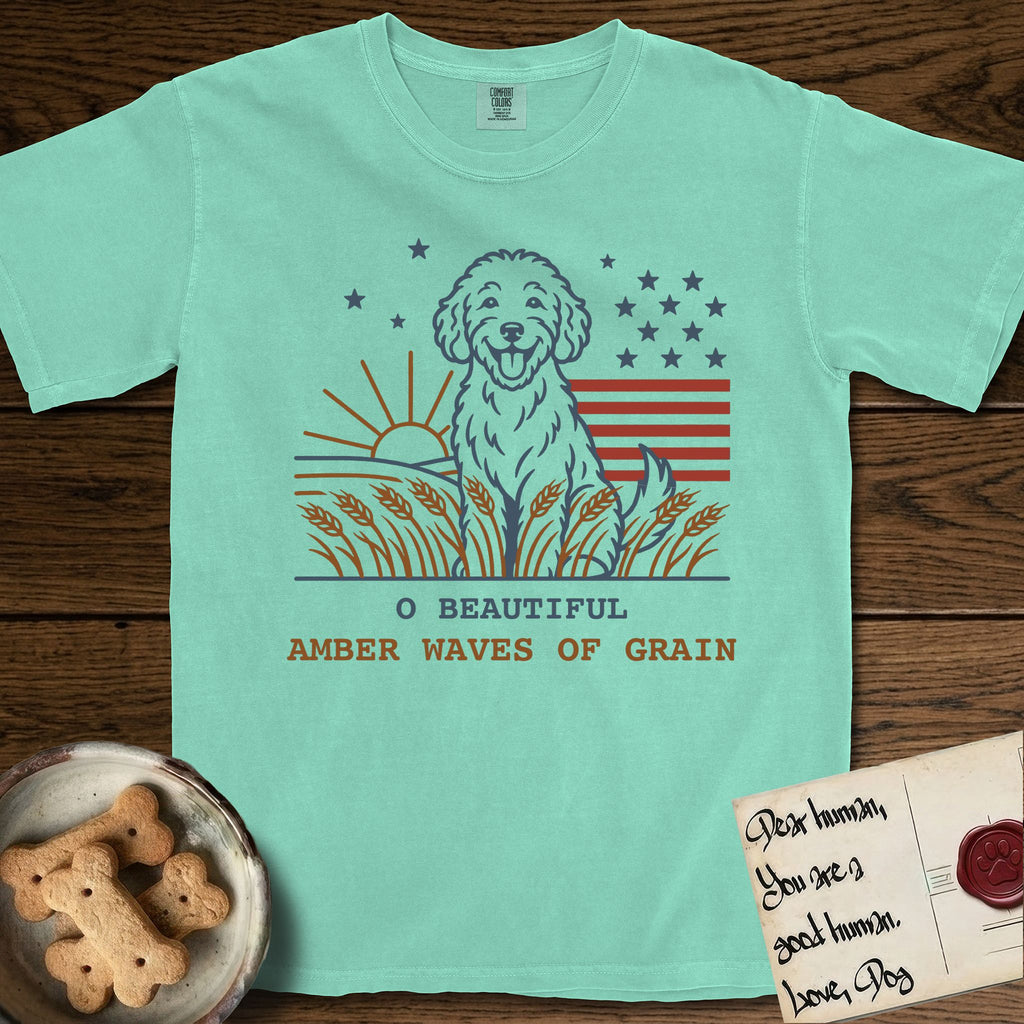 Amber Waves of Grain T-Shirt flat lay in Island Reef, featuring a faded vintage-Americana line-art Goldendoodle sitting in a wheat field with a rising sun, scattered stars, and red flag stripes, above “O Beautiful / Amber Waves of Grain” lettering.