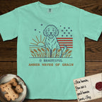 Amber Waves of Grain T-Shirt flat lay in Island Reef, featuring a faded vintage-Americana line-art Goldendoodle sitting in a wheat field with a rising sun, scattered stars, and red flag stripes, above “O Beautiful / Amber Waves of Grain” lettering.