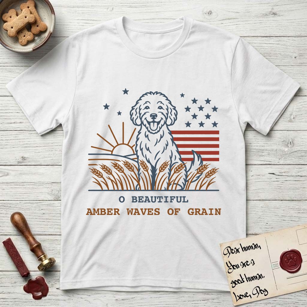 Amber Waves of Grain T-Shirt flat lay in White, featuring a faded vintage-Americana line-art Goldendoodle sitting in a wheat field with a rising sun, scattered stars, and red flag stripes, above “O Beautiful / Amber Waves of Grain” lettering.