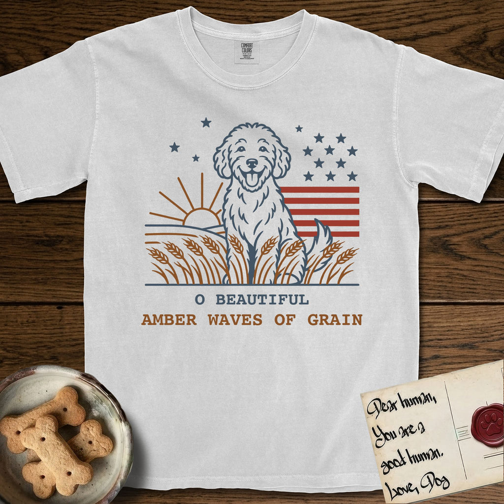 Amber Waves of Grain T-Shirt flat lay in White, featuring a faded vintage-Americana line-art Goldendoodle sitting in a wheat field with a rising sun, scattered stars, and red flag stripes, above “O Beautiful / Amber Waves of Grain” lettering.