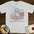 Amber Waves of Grain T-Shirt flat lay in White, featuring a faded vintage-Americana line-art Goldendoodle sitting in a wheat field with a rising sun, scattered stars, and red flag stripes, above “O Beautiful / Amber Waves of Grain” lettering.