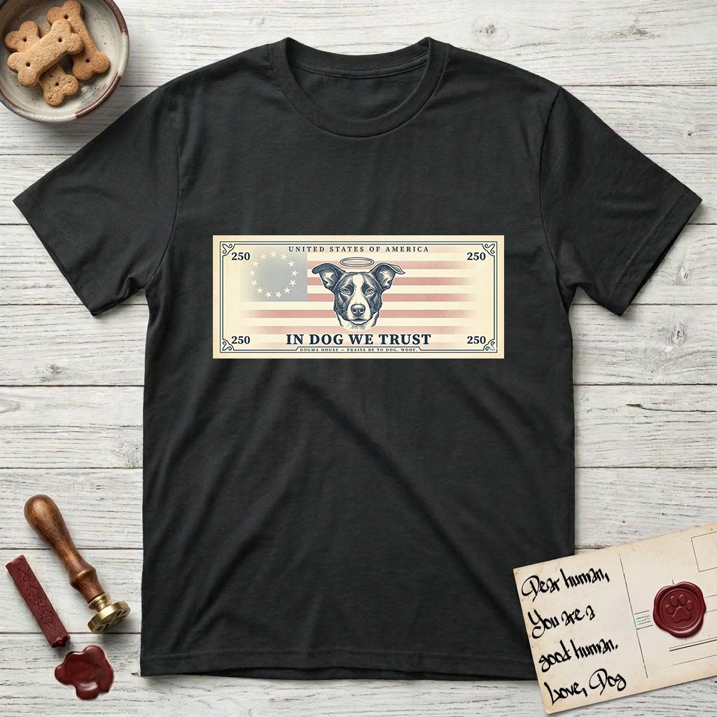 In Dog We Trust Bill T-Shirt flat lay in Black, featuring a vintage dollar-bill design with a haloed mixed-breed Dog at center, a Betsy Ross flag in the background, and bold currency-style "In Dog We Trust" typography.