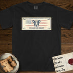 In Dog We Trust Bill T-Shirt flat lay in Black, featuring a vintage dollar-bill design with a haloed mixed-breed Dog at center, a Betsy Ross flag in the background, and bold currency-style "In Dog We Trust" typography.