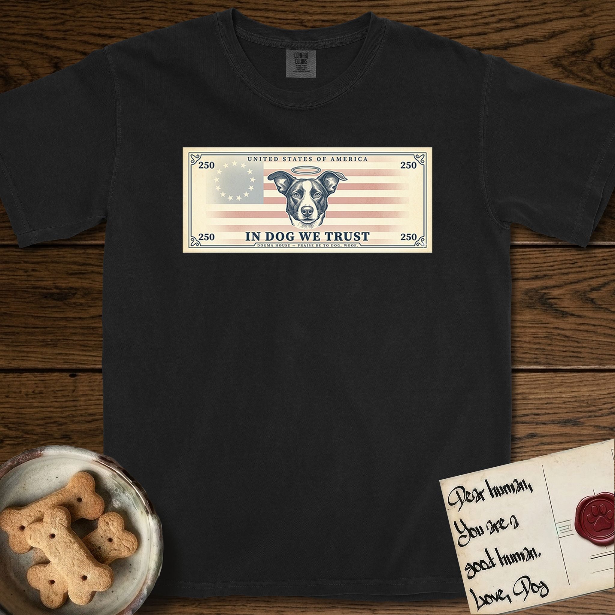 In Dog We Trust Bill T-Shirt flat lay in Black, featuring a vintage dollar-bill design with a haloed mixed-breed Dog at center, a Betsy Ross flag in the background, and bold currency-style "In Dog We Trust" typography.