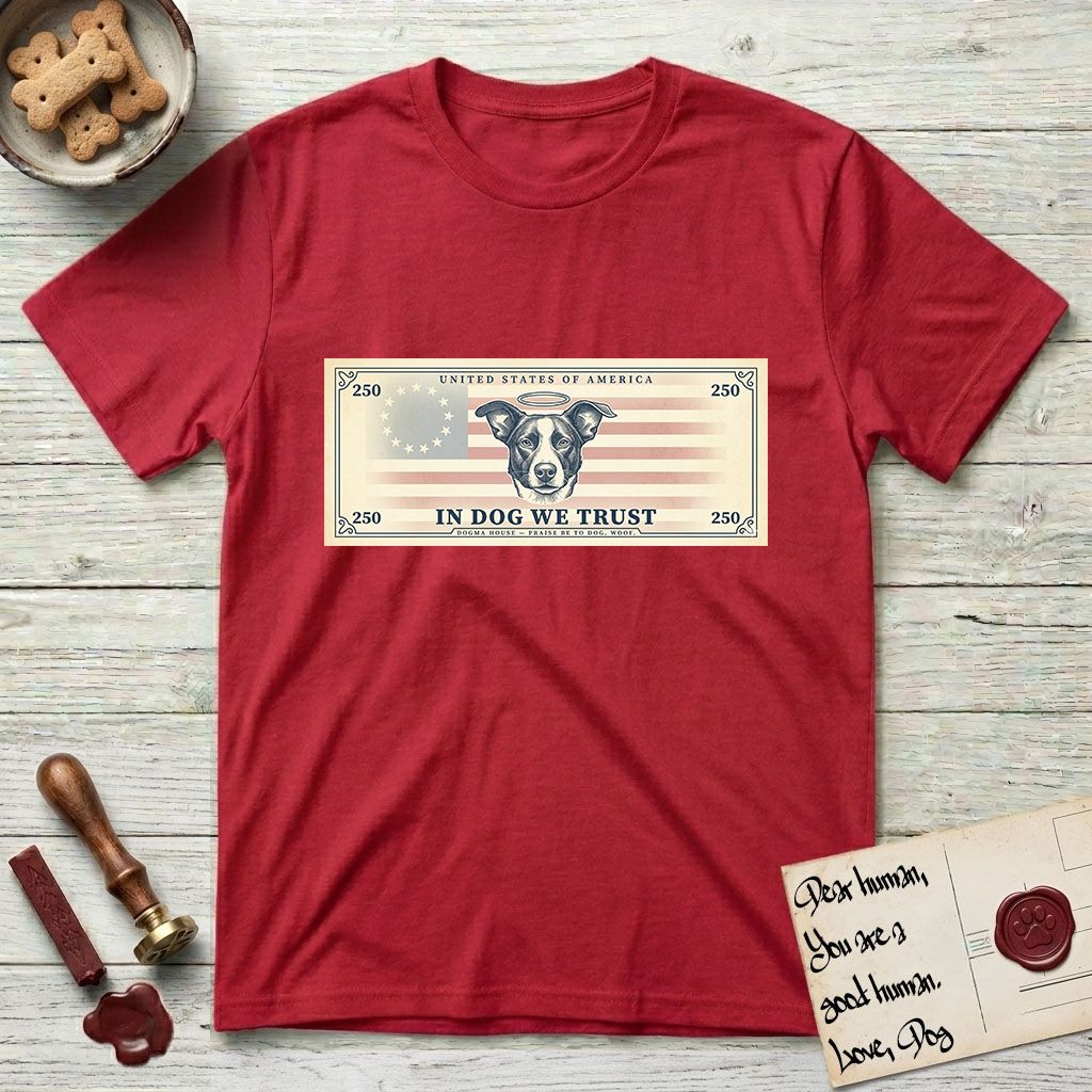 In Dog We Trust Bill T-Shirt flat lay in Cherry Red, featuring a vintage dollar-bill design with a haloed mixed-breed Dog at center, a Betsy Ross flag in the background, and bold currency-style "In Dog We Trust" typography.