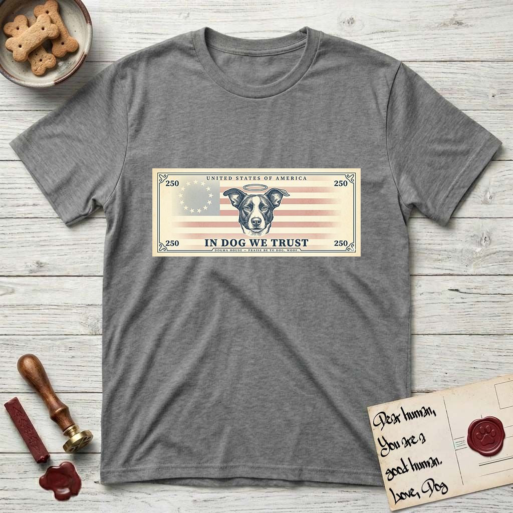 In Dog We Trust Bill T-Shirt flat lay in Graphite Heather, featuring a vintage dollar-bill design with a haloed mixed-breed Dog at center, a Betsy Ross flag in the background, and bold currency-style "In Dog We Trust" typography.