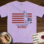 Let Freedom Ring T-Shirt flat lay in Orchid, featuring a faded vintage-Americana line-art Beagle sitting and baying with her head thrown back in front of red flag stripes, above “Let Freedom Ring” lettering.
