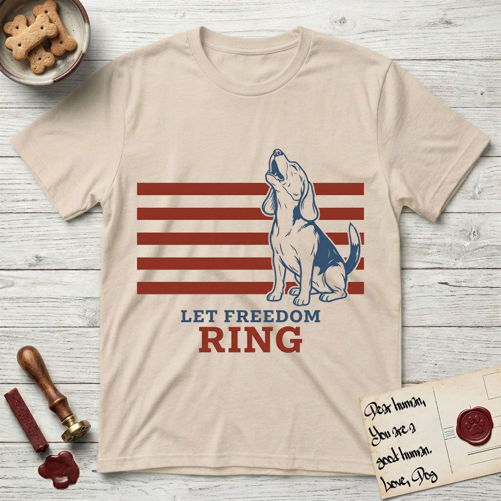 Let Freedom Ring T-Shirt flat lay in Sand, featuring a faded vintage-Americana line-art Beagle sitting and baying with her head thrown back in front of red flag stripes, above “Let Freedom Ring” lettering.