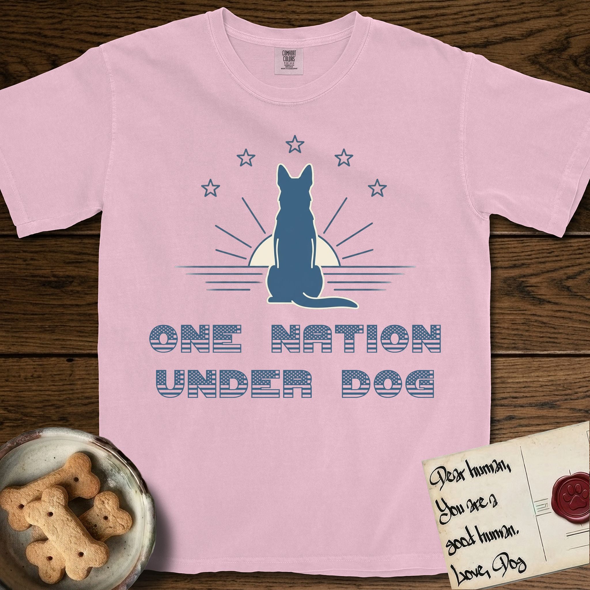 One Nation Under Dog T-Shirt flat lay in Blossom, featuring a minimalist design with a Dog silhouette over a radiating sunburst, five stars, and bold "One Nation Under Dog" typography.