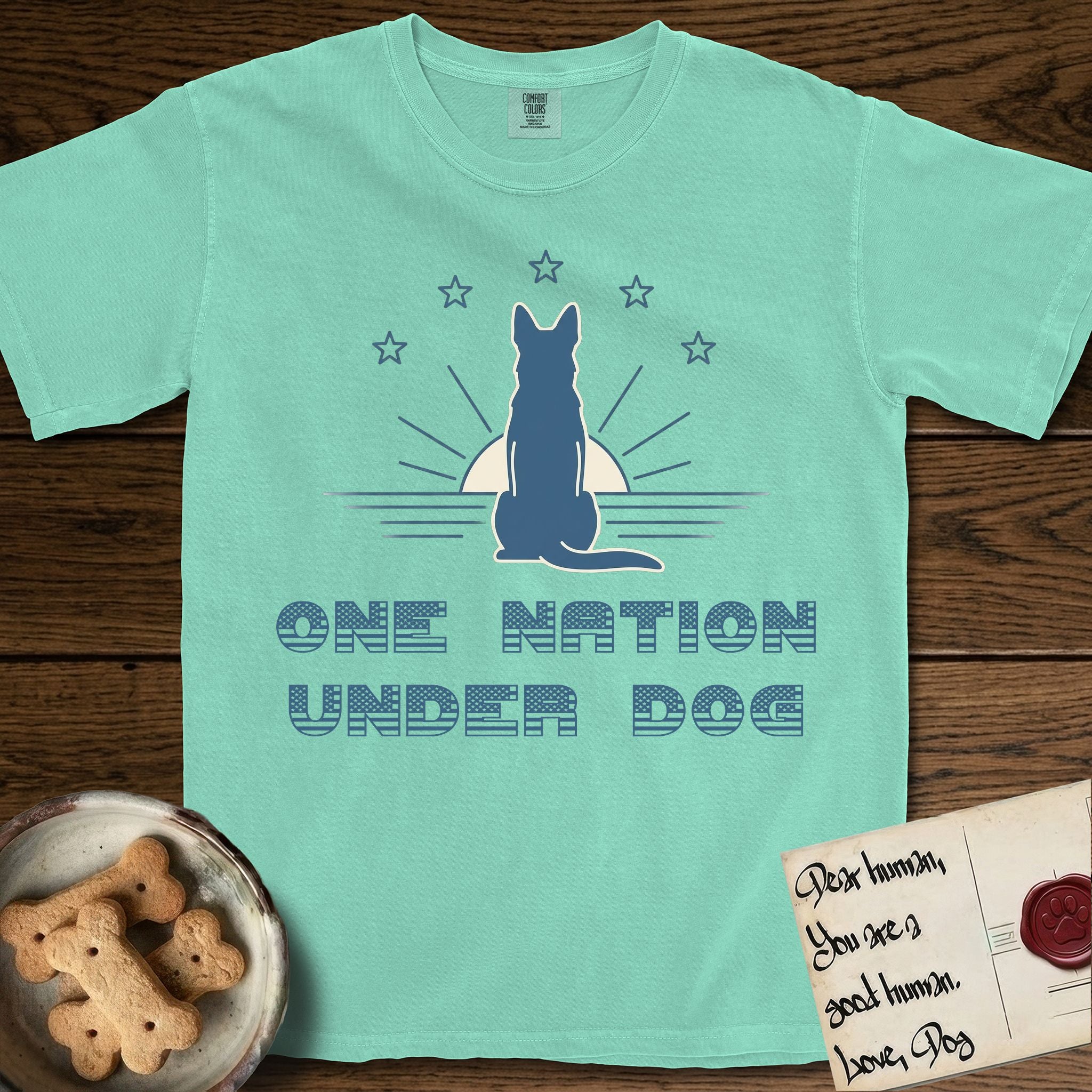 One Nation Under Dog T-Shirt flat lay in Island Reef, featuring a minimalist design with a Dog silhouette over a radiating sunburst, five stars, and bold "One Nation Under Dog" typography.