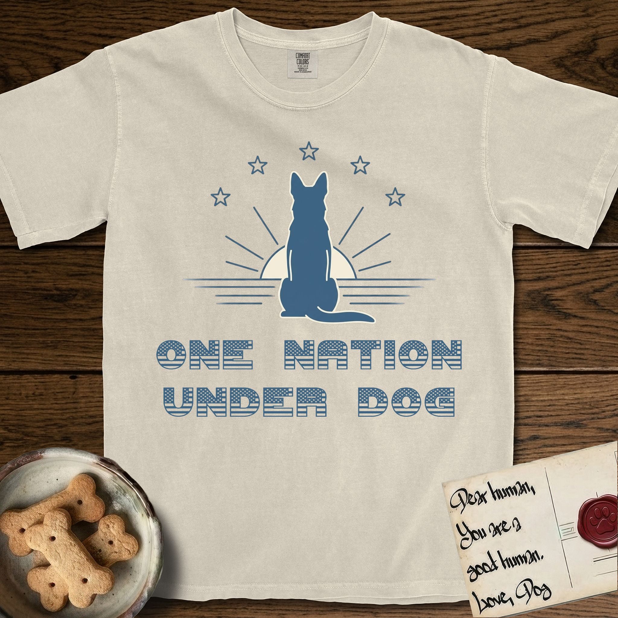 One Nation Under Dog T-Shirt flat lay in Ivory, featuring a minimalist design with a Dog silhouette over a radiating sunburst, five stars, and bold "One Nation Under Dog" typography.