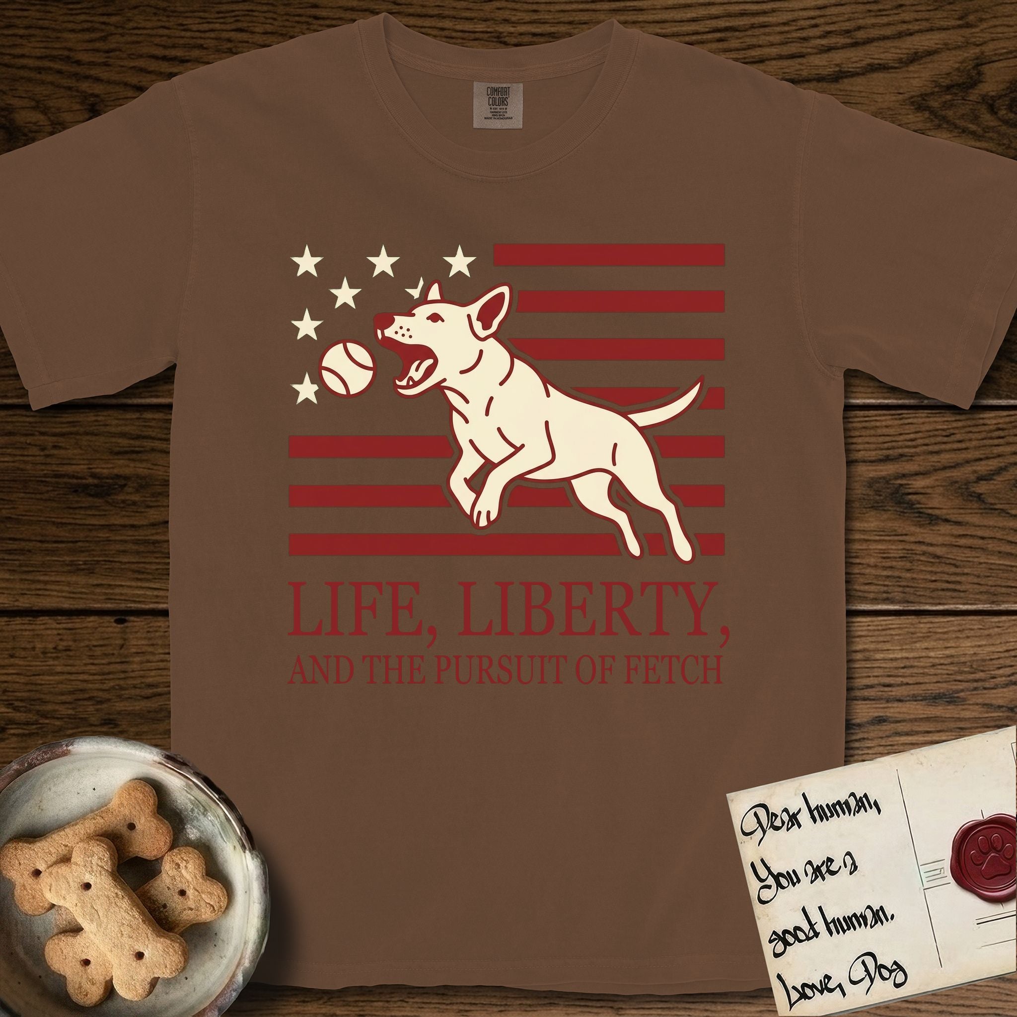Life, Liberty, and the Pursuit of Fetch T-Shirt flat lay in Espresso, featuring a square flag-inspired design with a Bull Terrier leaping after a ball, cream stars, and bold "Life, Liberty, and the Pursuit of Fetch" serif typography.