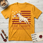 Life, Liberty, and the Pursuit of Fetch T-Shirt flat lay in Gold, featuring a square flag-inspired design with a Bull Terrier leaping after a ball, cream stars, and bold "Life, Liberty, and the Pursuit of Fetch" serif typography.