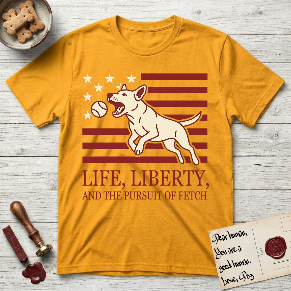 Life, Liberty, and the Pursuit of Fetch T-Shirt flat lay in Gold, featuring a square flag-inspired design with a Bull Terrier leaping after a ball, cream stars, and bold "Life, Liberty, and the Pursuit of Fetch" serif typography.