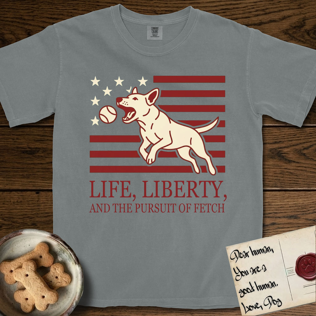 Life, Liberty, and the Pursuit of Fetch T-Shirt flat lay in Granite, featuring a square flag-inspired design with a Bull Terrier leaping after a ball, cream stars, and bold "Life, Liberty, and the Pursuit of Fetch" serif typography.