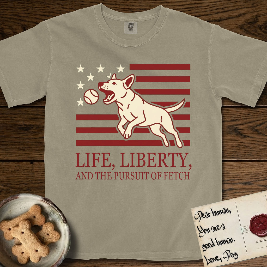 Life, Liberty, and the Pursuit of Fetch T-Shirt flat lay in Khaki, featuring a square flag-inspired design with a Bull Terrier leaping after a ball, cream stars, and bold "Life, Liberty, and the Pursuit of Fetch" serif typography.