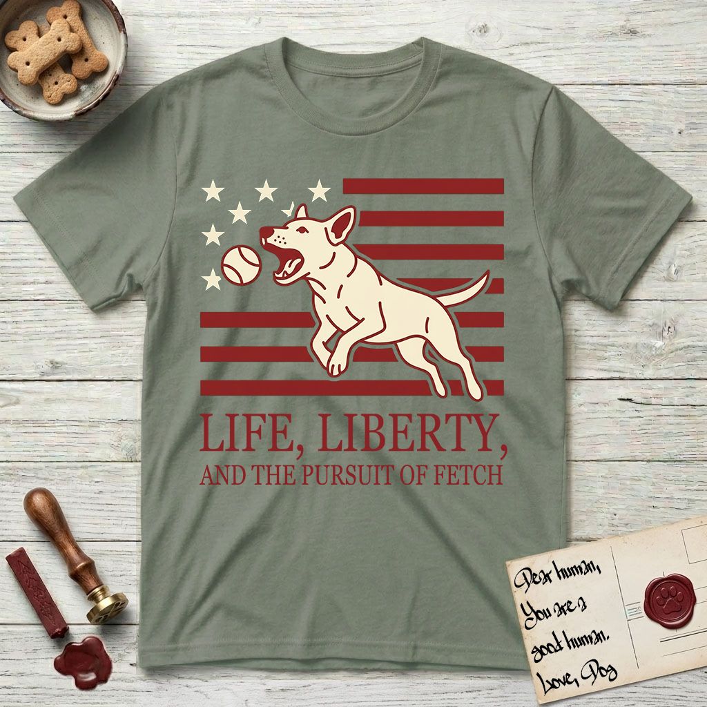 Life, Liberty, and the Pursuit of Fetch T-Shirt flat lay in Sage, featuring a square flag-inspired design with a Bull Terrier leaping after a ball, cream stars, and bold "Life, Liberty, and the Pursuit of Fetch" serif typography.