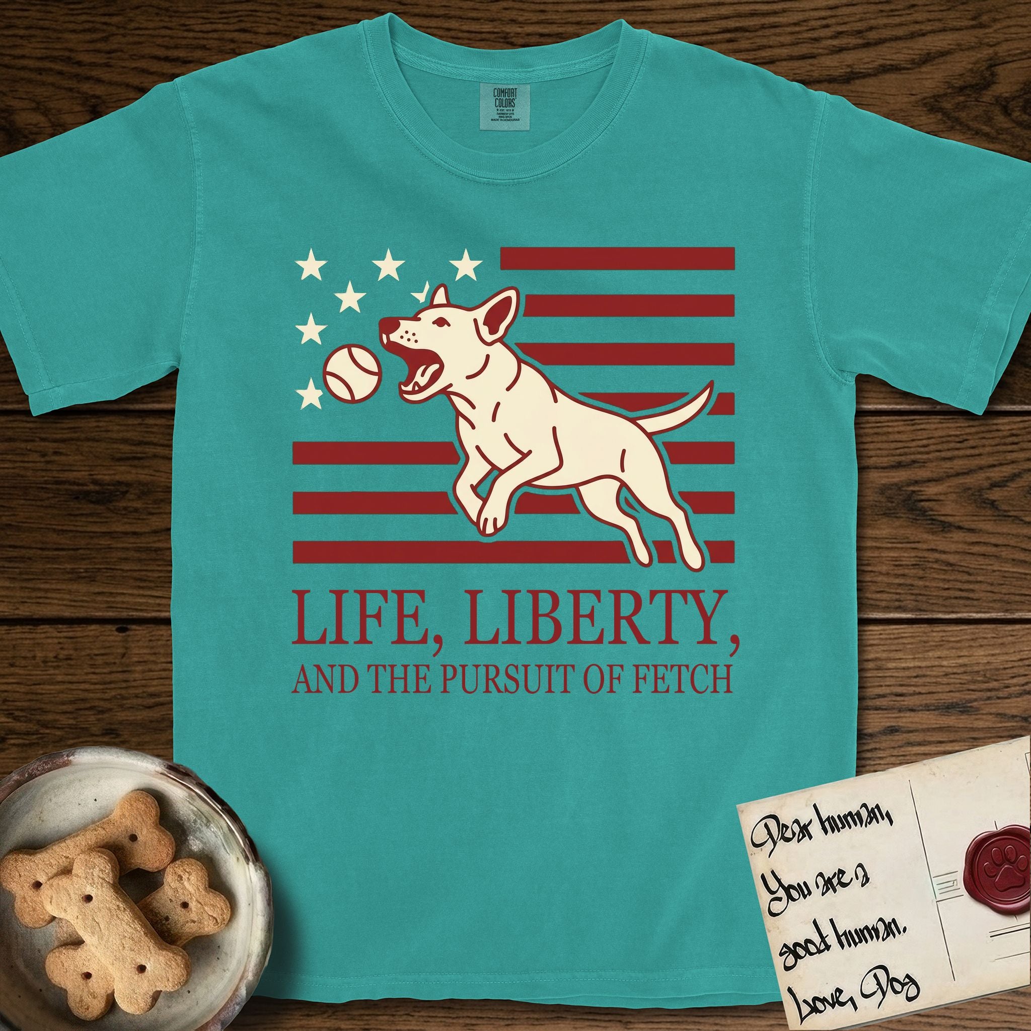 Life, Liberty, and the Pursuit of Fetch T-Shirt flat lay in Seafoam, featuring a square flag-inspired design with a Bull Terrier leaping after a ball, cream stars, and bold "Life, Liberty, and the Pursuit of Fetch" serif typography.