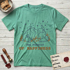 The Pursuit of Happiness T-Shirt flat lay in Heather Irish Green, featuring a faded vintage-Americana line-art Samoyed rolling on his back in the grass with paws in the air under a sky of stars, above “The Pursuit of Happiness” lettering.