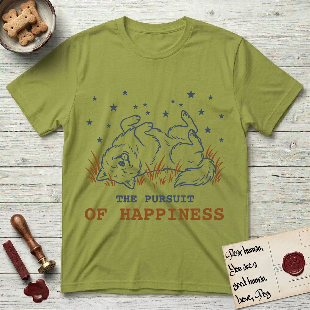 The Pursuit of Happiness T-Shirt flat lay in Kiwi, featuring a faded vintage-Americana line-art Samoyed rolling on his back in the grass with paws in the air under a sky of stars, above “The Pursuit of Happiness” lettering.