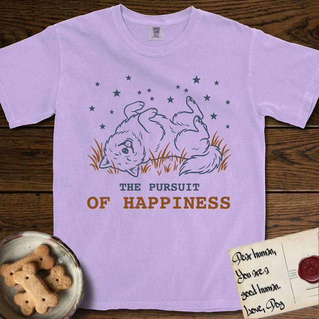 The Pursuit of Happiness T-Shirt flat lay in Orchid, featuring a faded vintage-Americana line-art Samoyed rolling on his back in the grass with paws in the air under a sky of stars, above “The Pursuit of Happiness” lettering.