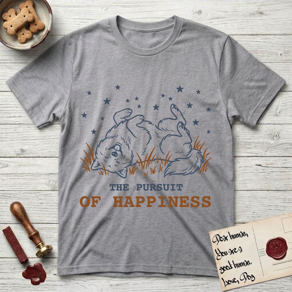The Pursuit of Happiness T-Shirt flat lay in Sport Grey, featuring a faded vintage-Americana line-art Samoyed rolling on his back in the grass with paws in the air under a sky of stars, above “The Pursuit of Happiness” lettering.