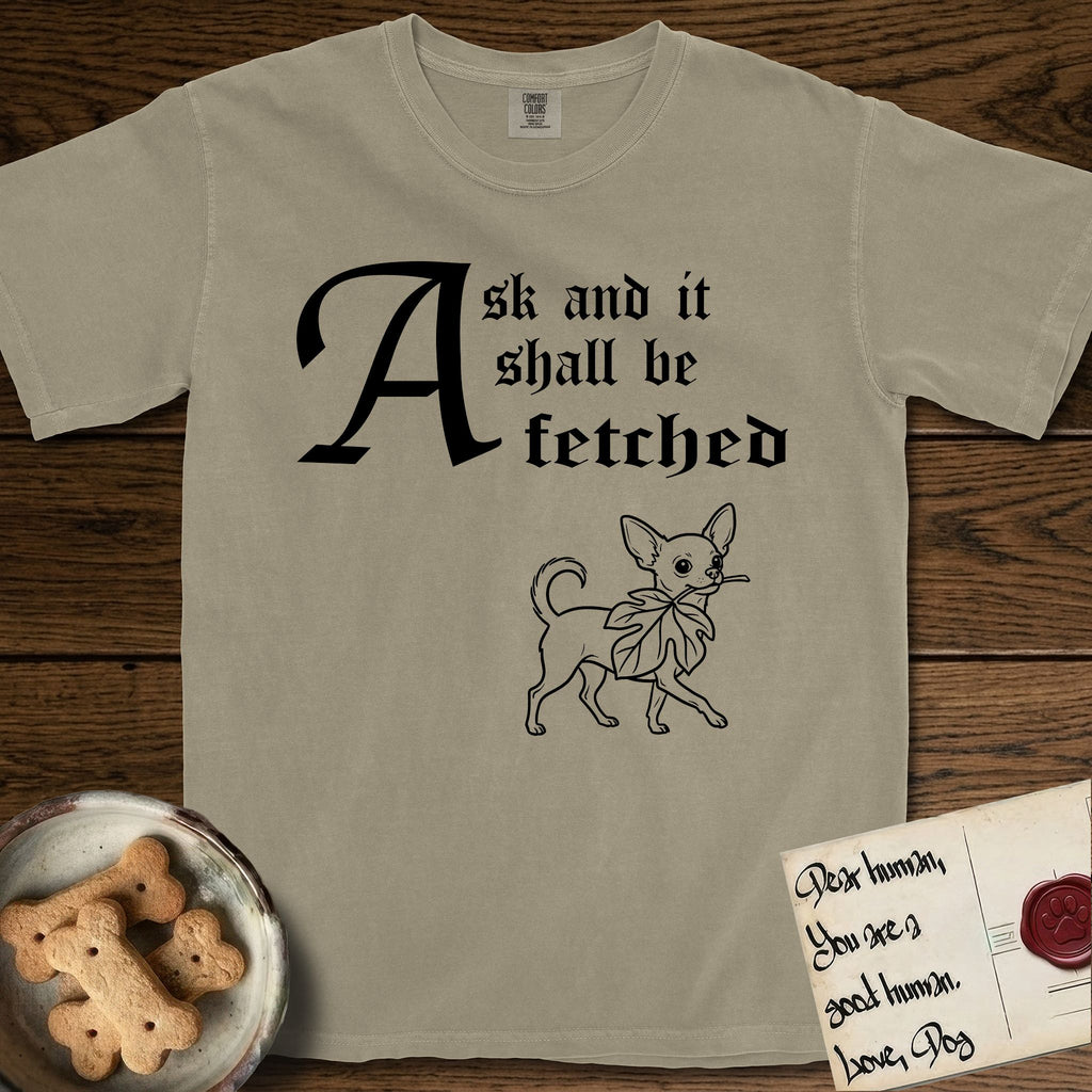 Ask and It Shall Be Fetched Chihuahua T-Shirt flat lay in Khaki, featuring a sparse pen-and-ink illustration of a Chihuahua at a proud trot carrying an oversized fig leaf.