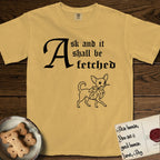 Ask and It Shall Be Fetched Chihuahua T-Shirt flat lay in Mustard, featuring a sparse pen-and-ink illustration of a Chihuahua at a proud trot carrying an oversized fig leaf.