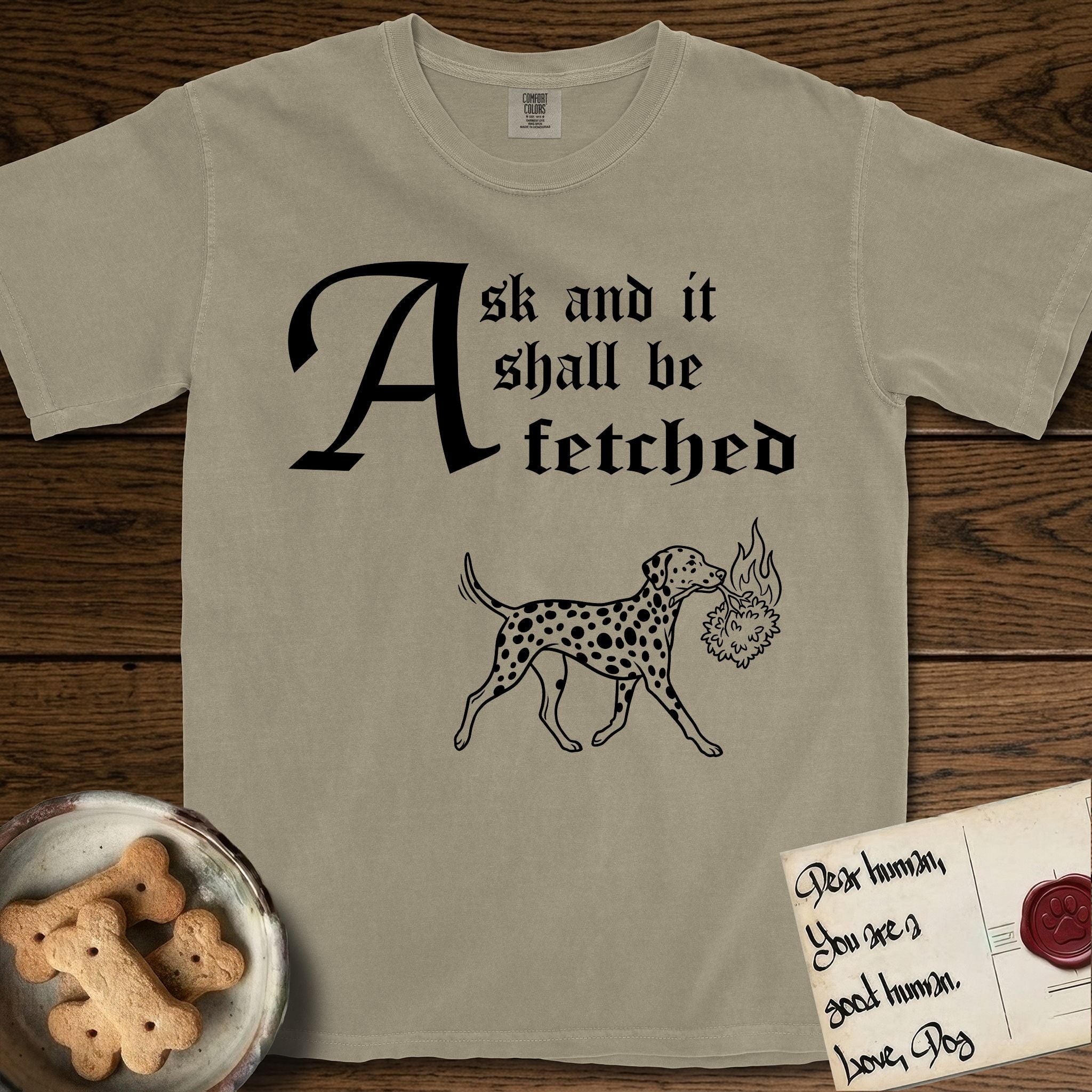 Ask and It Shall Be Fetched Dalmatian T-Shirt flat lay in Khaki, featuring a sparse pen-and-ink illustration of a Dalmatian at a proud trot carrying a small burning bush.