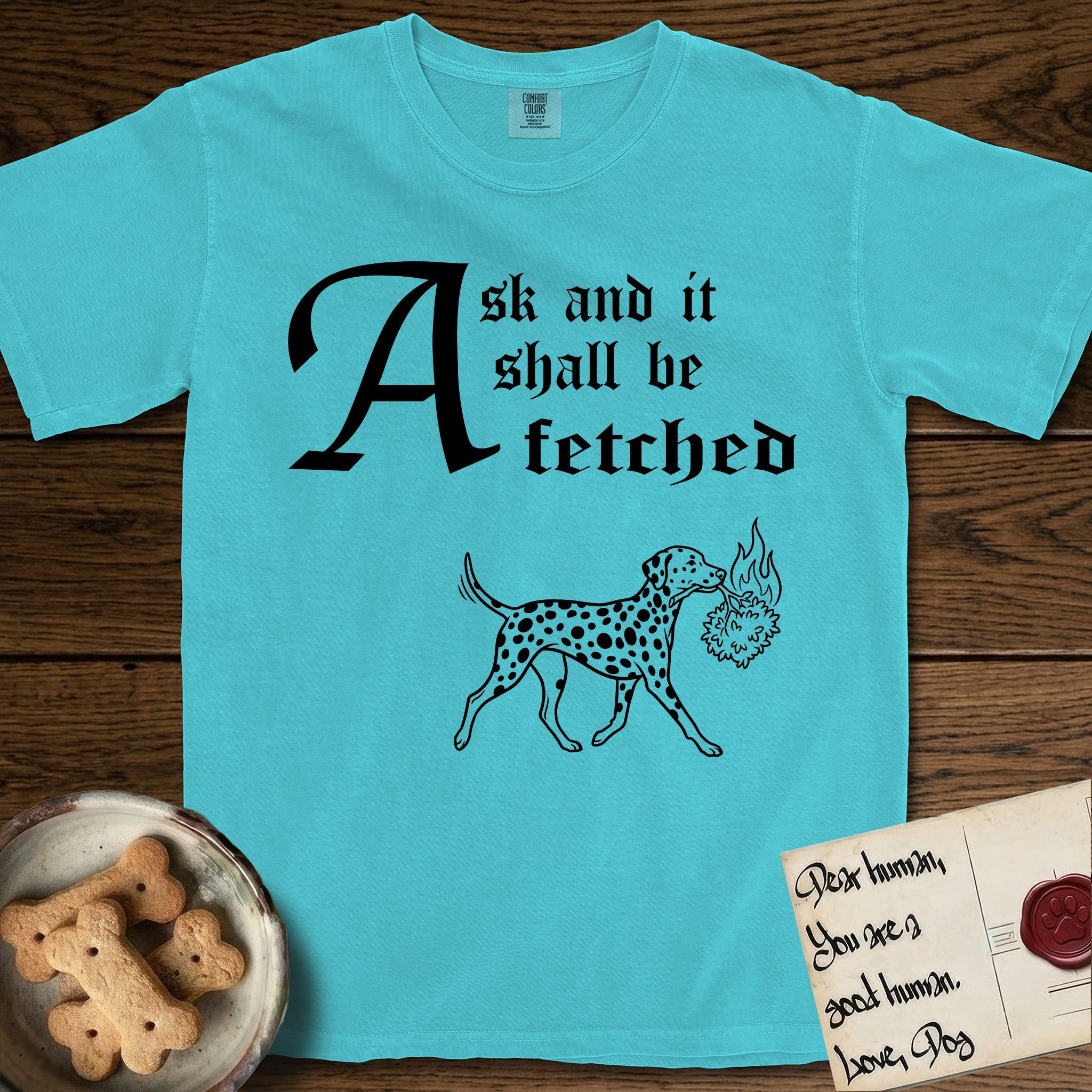 Ask and It Shall Be Fetched Dalmatian T-Shirt flat lay in Lagoon Blue, featuring a sparse pen-and-ink illustration of a Dalmatian at a proud trot carrying a small burning bush.
