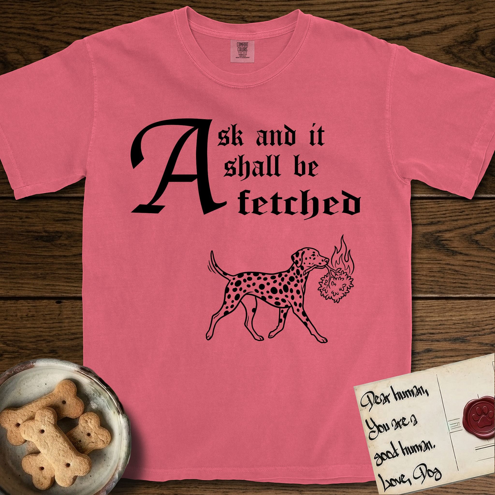 Ask and It Shall Be Fetched Dalmatian T-Shirt flat lay in Watermelon, featuring a sparse pen-and-ink illustration of a Dalmatian at a proud trot carrying a small burning bush.