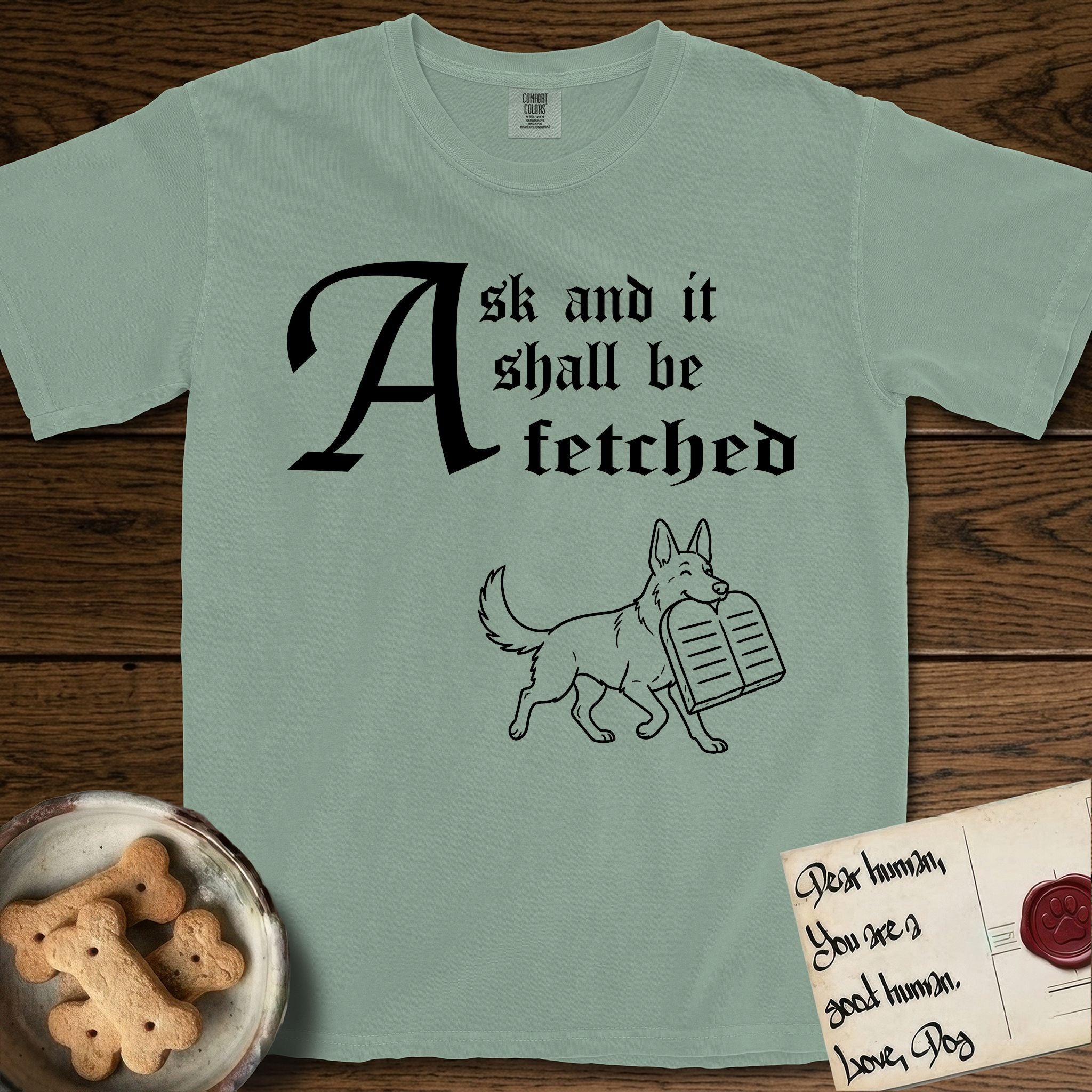 Ask and It Shall Be Fetched German Shepherd T-Shirt flat lay in Bay, featuring a sparse pen-and-ink illustration of a German Shepherd at a proud trot carrying a pair of stone tablets.