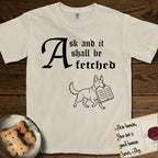Ask and It Shall Be Fetched German Shepherd T-Shirt flat lay in Ivory, featuring a sparse pen-and-ink illustration of a German Shepherd at a proud trot carrying a pair of stone tablets.